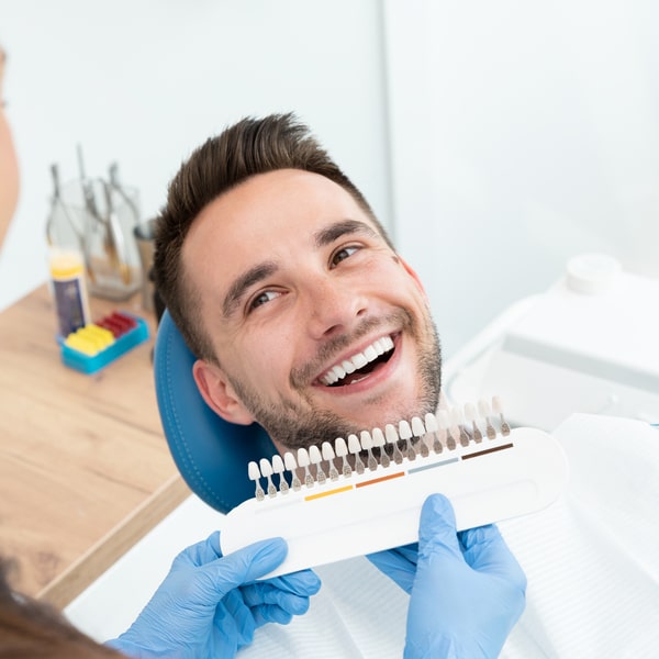 A man in a dental chair is smiling while the dentist shows him the color palette